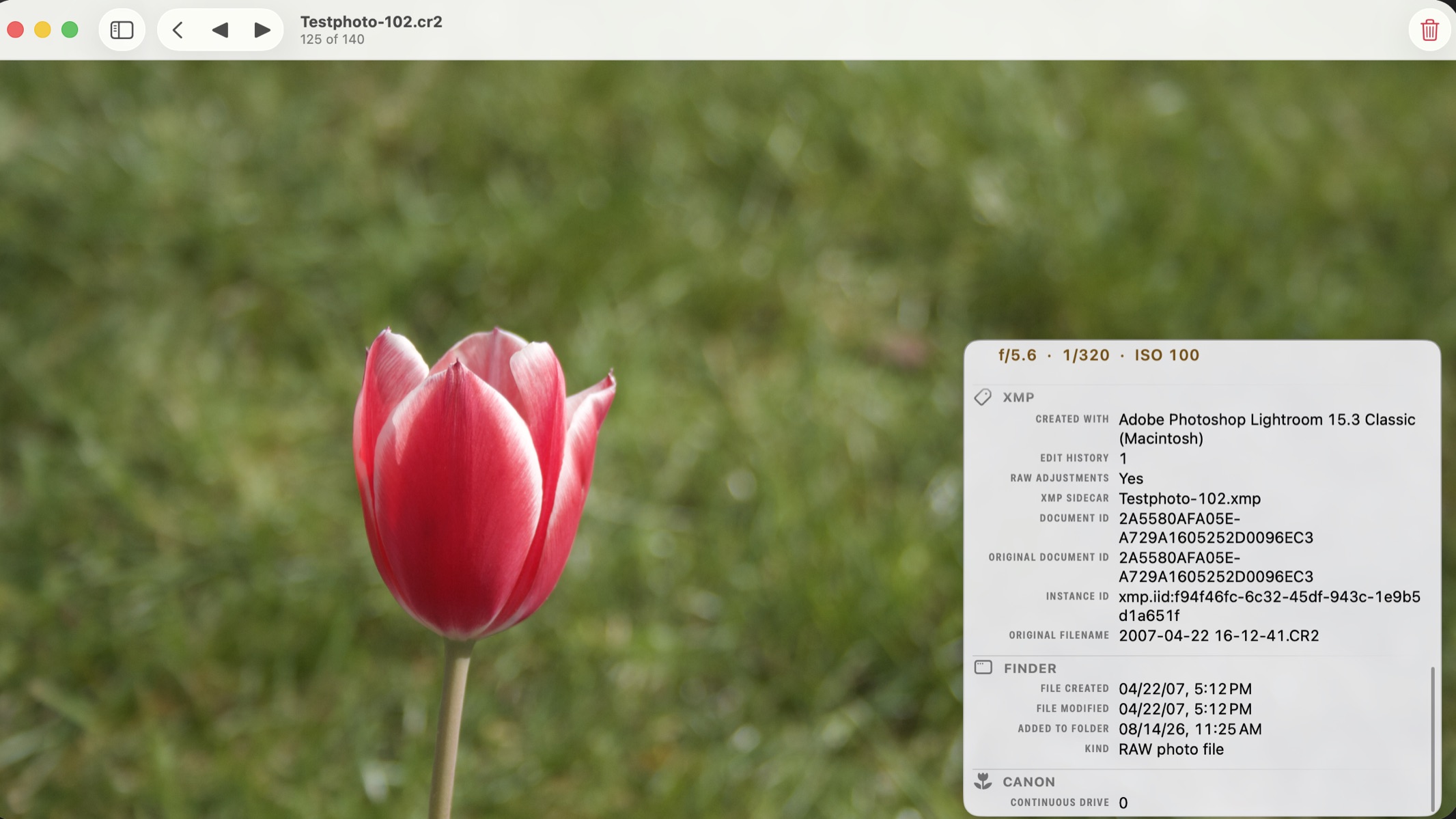 A red and white tulip in front of blurred grass, open in PhotoView on a Mac from the Canon RAW file Testphoto-102.cr2, with the metadata overlay on the right showing the XMP group: created with Adobe Photoshop Lightroom 15.3 Classic, one edit history step, RAW adjustments, and the XMP sidecar file Testphoto-102.xmp